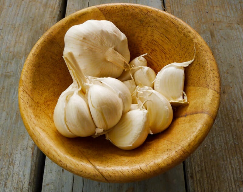 Three heads of homegrown white softneck garlic in a wooden bowl.