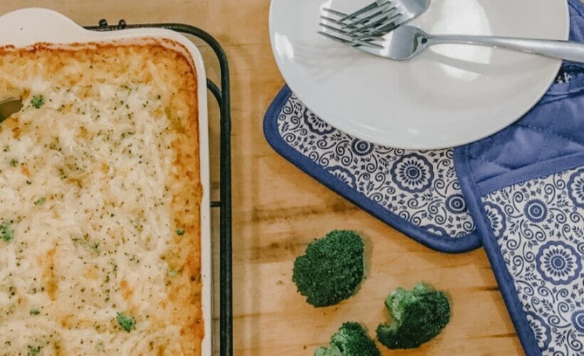 Broccoli rice casserole with loads of cheese in a casserole dish and oven mitts.