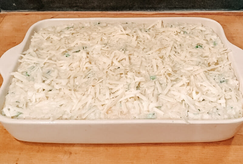 Assembled broccoli rice casserole in a cream colored dish and ready to go in the oven.