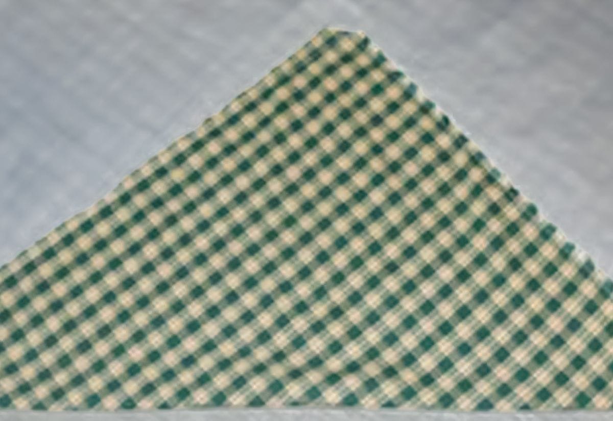 Green gingham apron fabric folded into a triangle for accurate cutting.