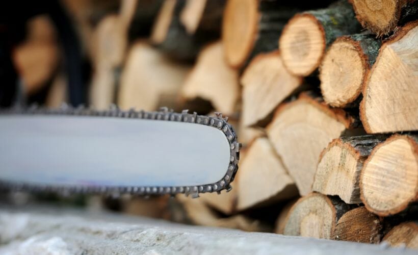 A chainsaw positioned in front of a pile of wood.