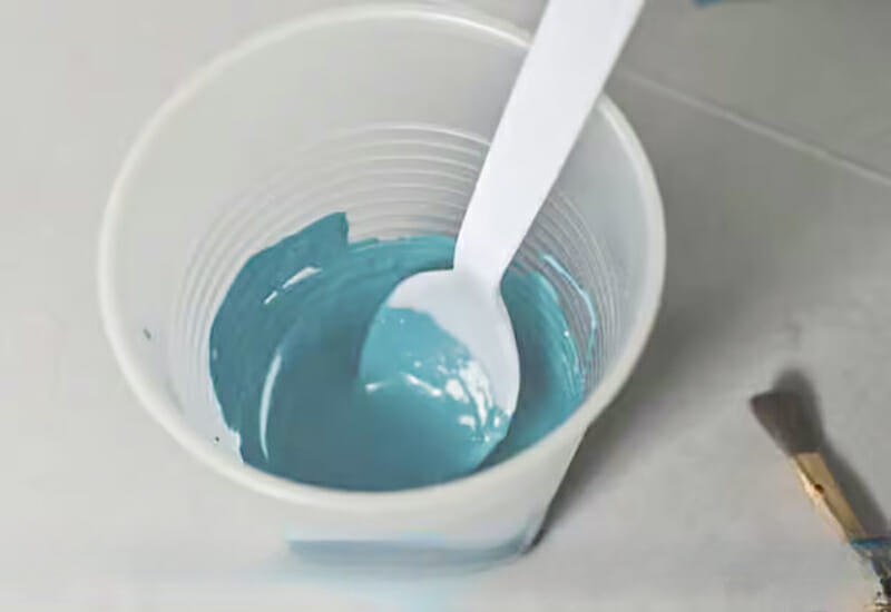 Stirring blue homemade chalkboard paint in a plastic cup with a plastic spoon.