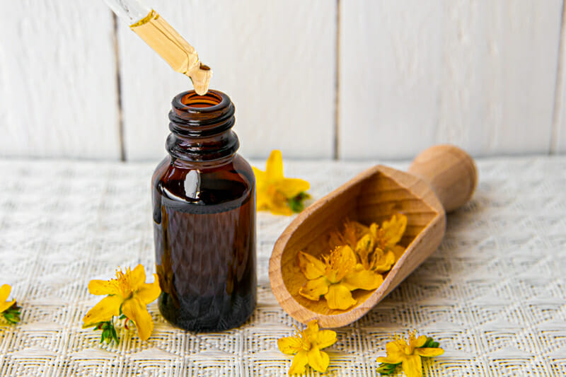 A floral tincture in an amber bottle surrounded by small yellow flowers.