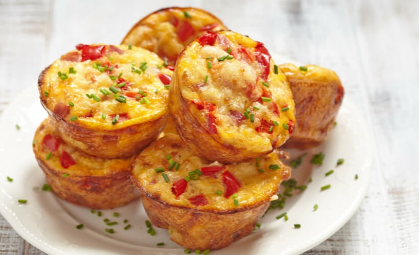 A white plate with red pepper, cheddar, and ham mini quiches topped with chopped chives.