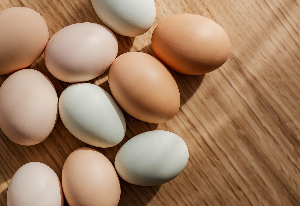 A collection of multicolored farm-fresh eggs in shades of brown, cream, and blue resting on a wooden table in natural light.