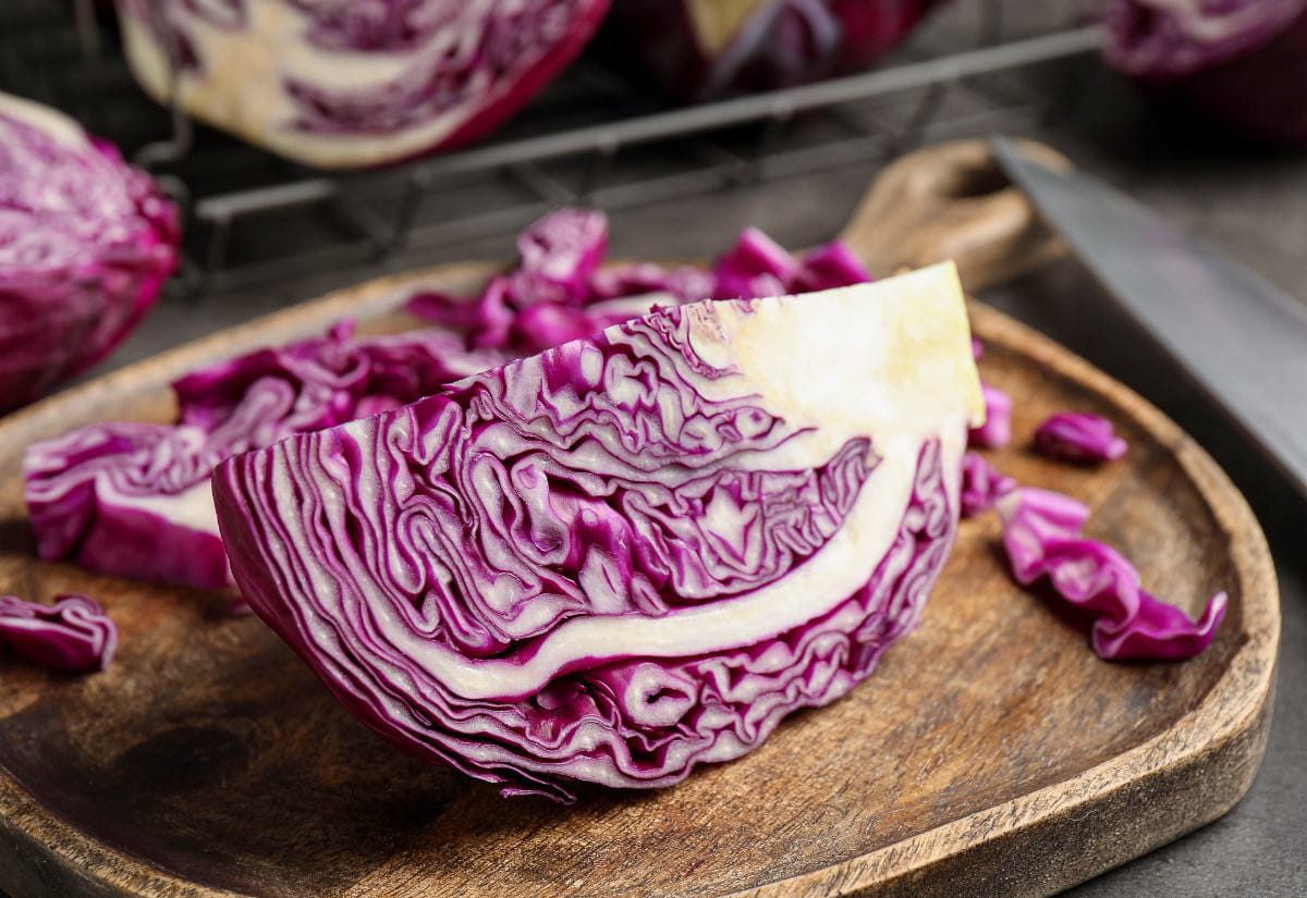 Cut wedge of red cabbage with vibrant purple and white layers sitting on a wooden cutting board, an ingredient commonly used to make natural blue egg dye.