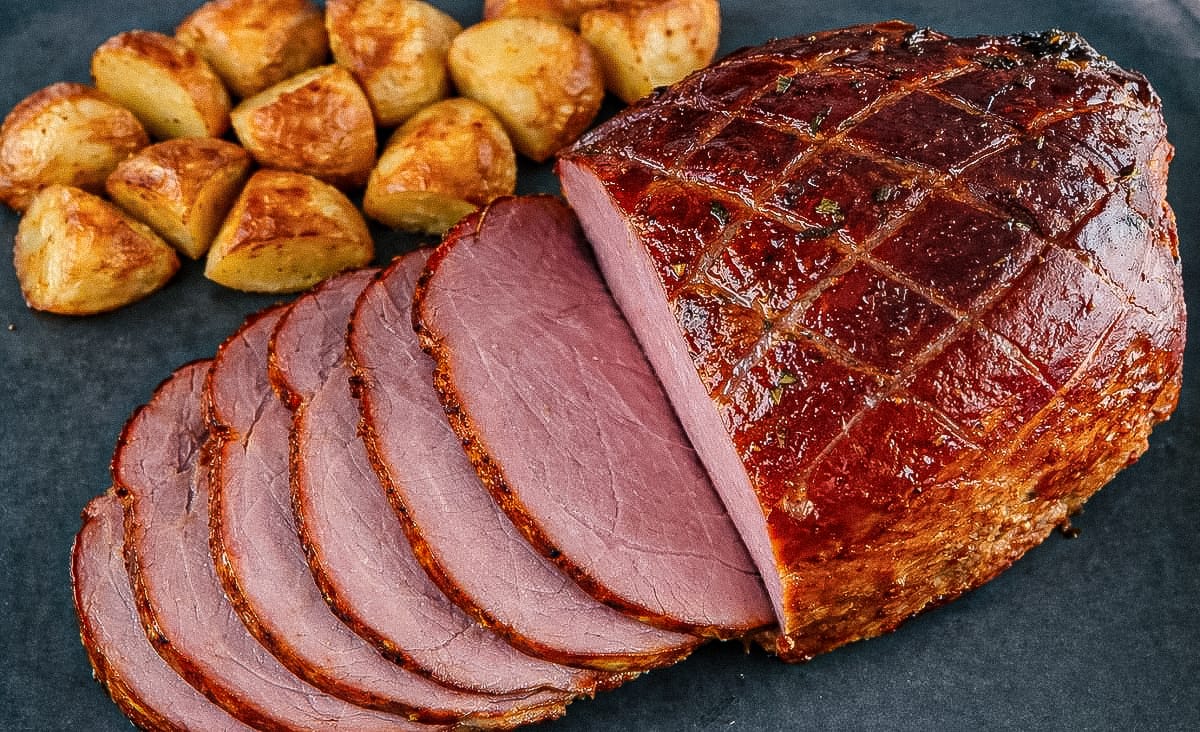 Sliced maple glazed ham with roasted potatoes arranged on a dark serving platter.