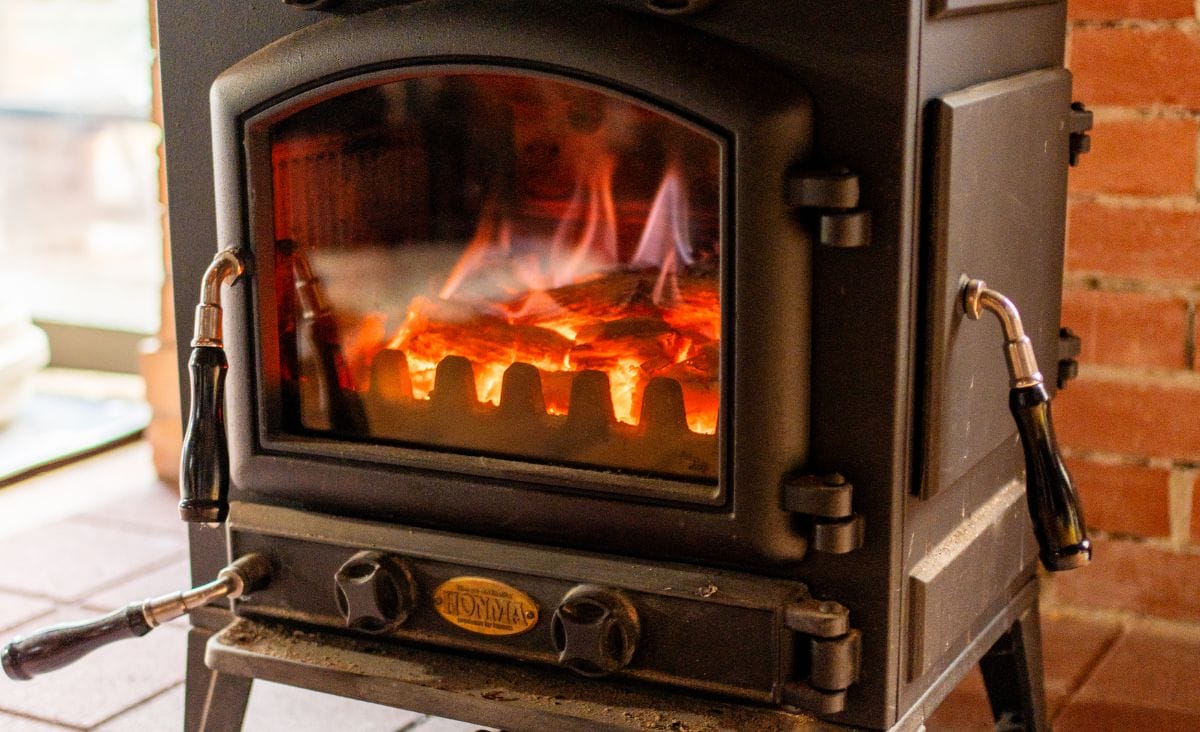 A cozy wood stove with clean glass showcasing a bright fire inside, warming a rustic brick and wood-paneled room.