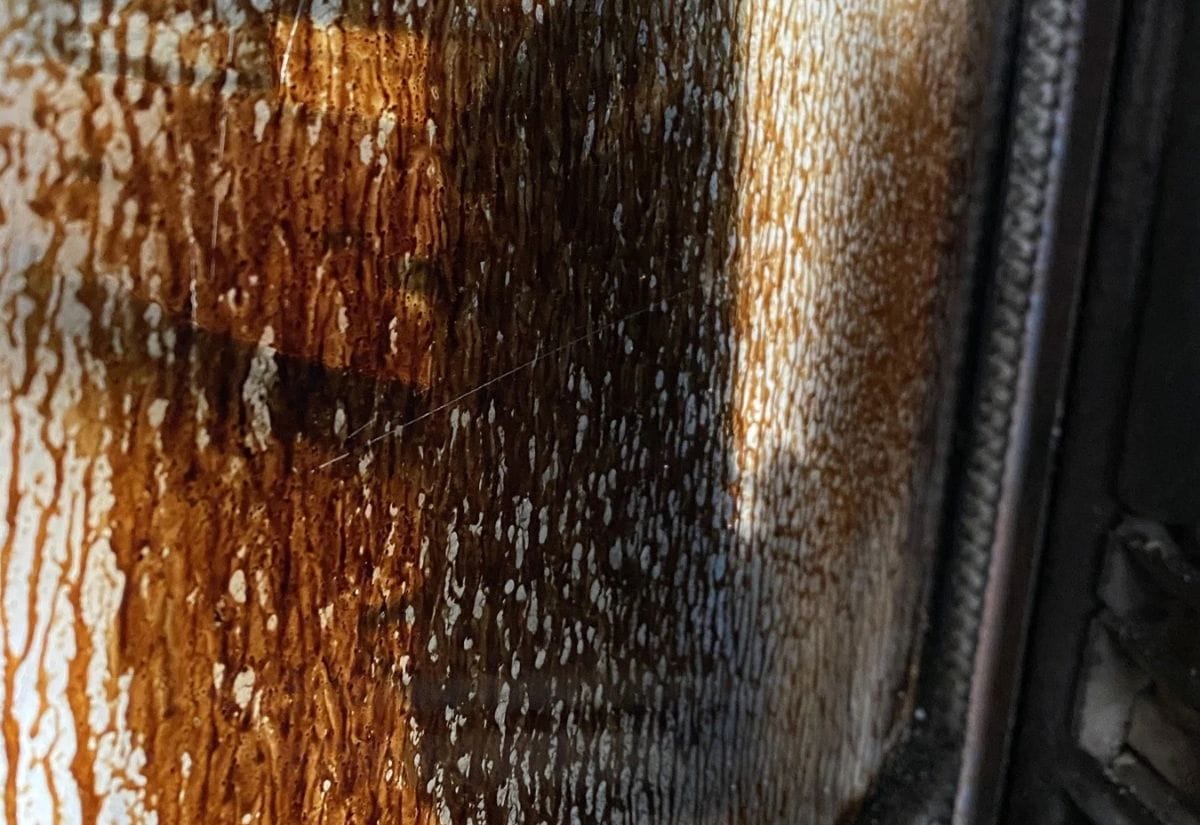 Close-up of heavily soiled wood stove glass covered in creosote and soot buildup.