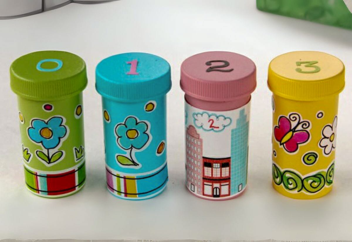 Four pill bottles decorated with colorful paper and stickers, numbered 0–3, used for holding piping tips by size.