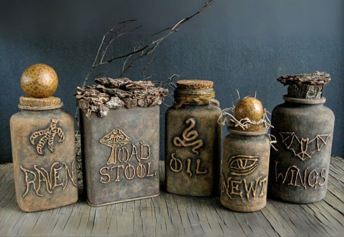 Five pill bottles transformed into spooky potion bottles with dark paint, bark tops, and carved labels like “Raven” and “Newt.”