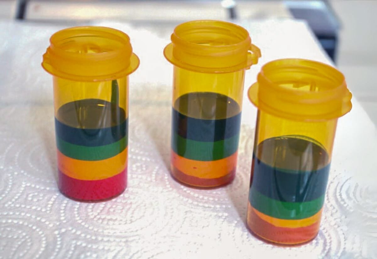 Three pill bottles filled with layers of melted crayon wax in rainbow colors, used as molds for homemade crayons.