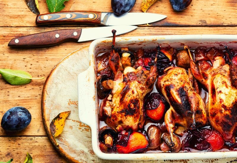 Roasted quail and vegetables in a casserole dish.