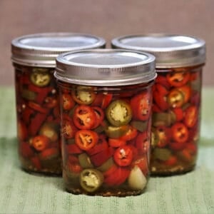 Three pint jars filled with sliced red and green pickled hot peppers in vinegar brine, a shelf-stable recipe for how to preserve hot peppers at home.