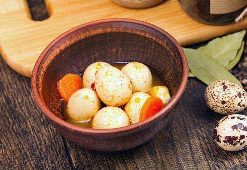 Pickled quail eggs with carrots in a wooden bowl.