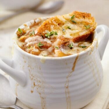 A white ceramic bowl of French Onion Soup that was caramelized in a slow cooker.