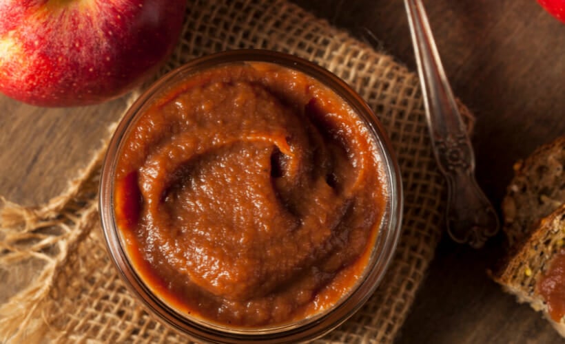 Apple butter in a jar with crab apples in the background.
