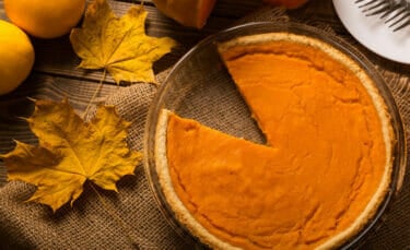 A pumpkin pie with a slice missing and leaves and tiny pumpkins around it.