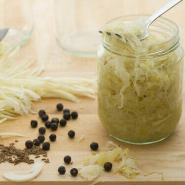 A jar of homemade sauerkraut surrounded by the ingredients to make it.