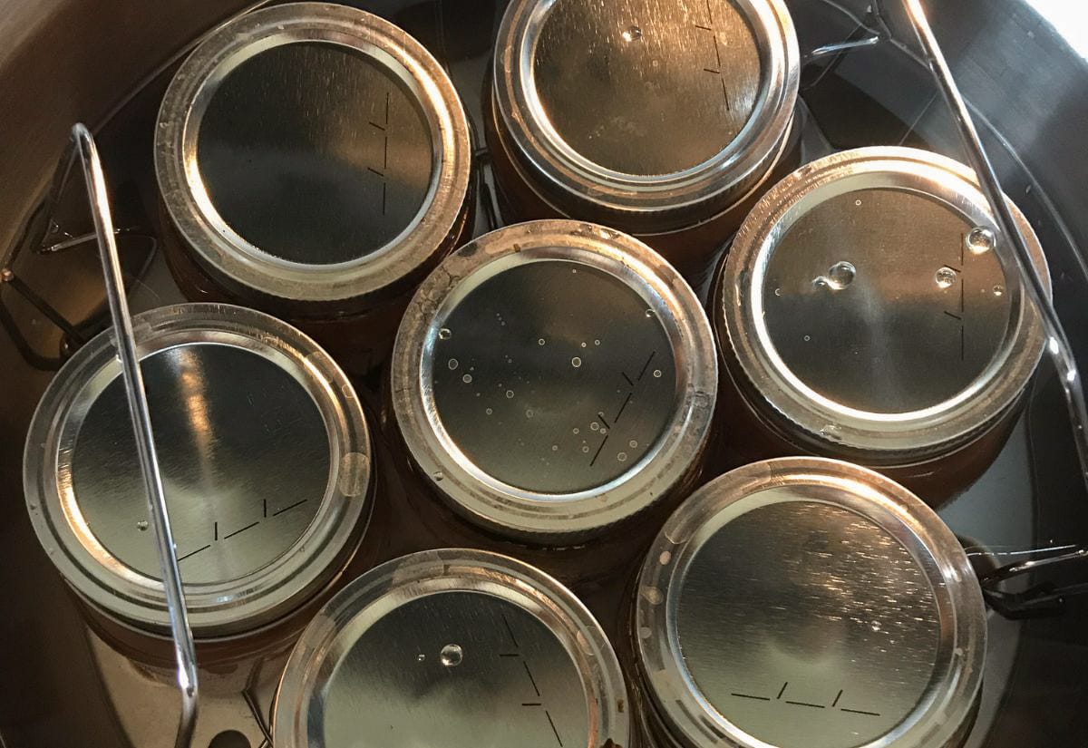 Top view of sealed canning jars filled with crabapple butter inside a boiling water bath canner, ready for processing.