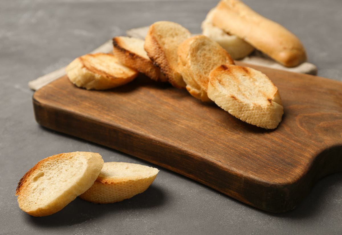 Golden toasted baguette slices resting on a wooden cutting board, ready to top the French onion soup.