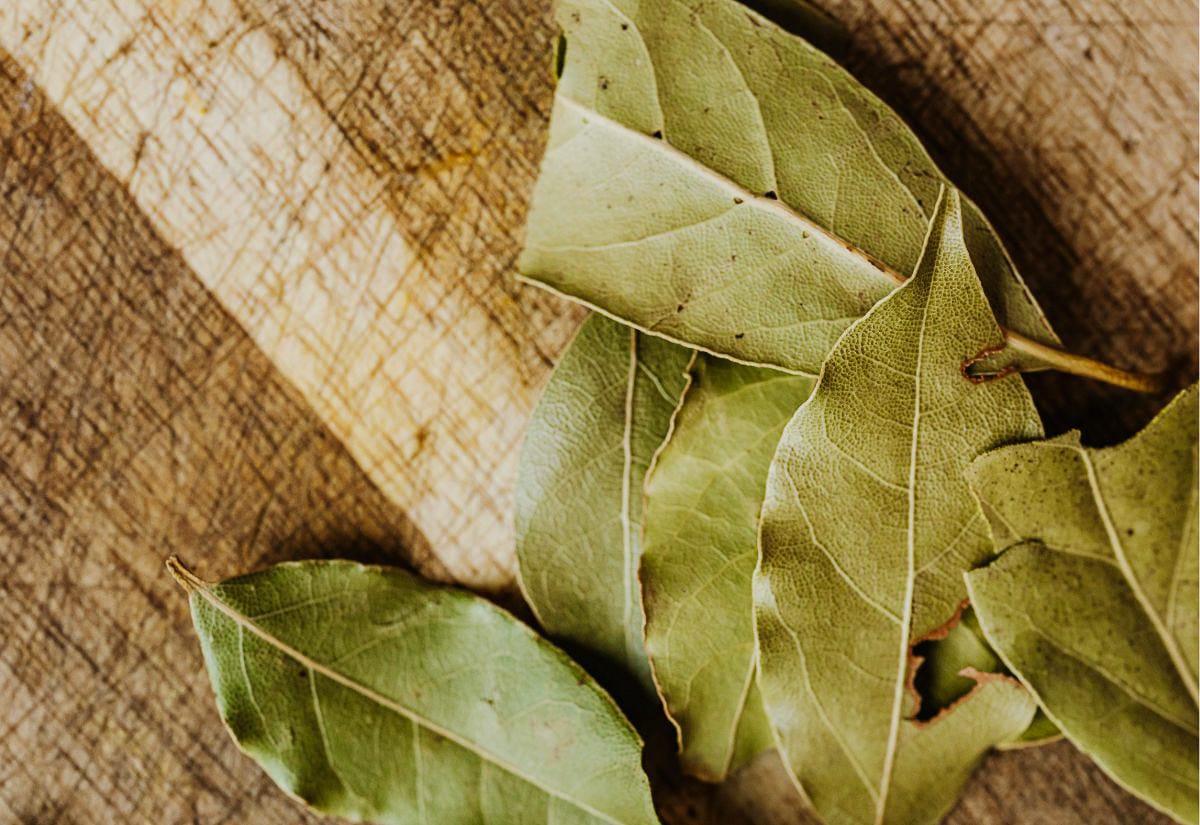 Dried bay leaves scattered on a worn wooden cutting board, showing texture and warm natural light.