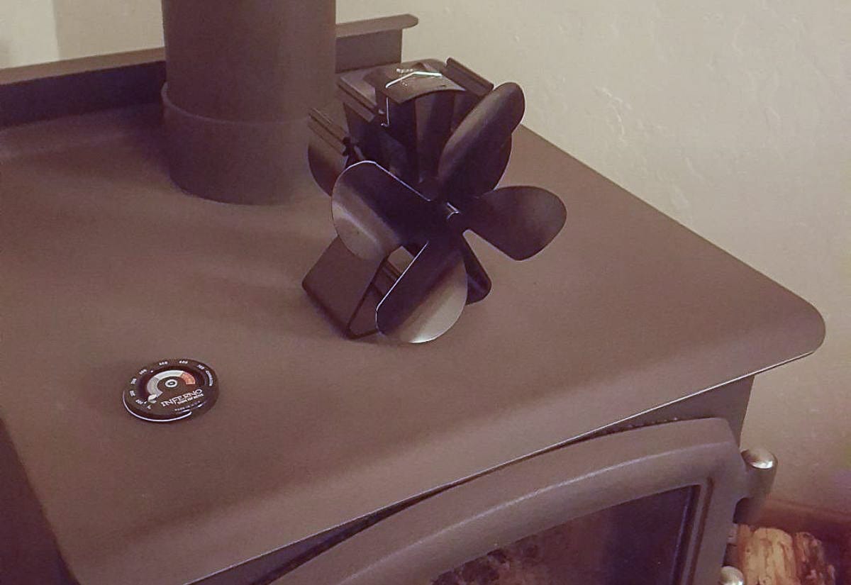 Black heat-powered stove fan on a cast-iron wood stove, showing the fan blades and base clearly for a detailed look at how the device operates.