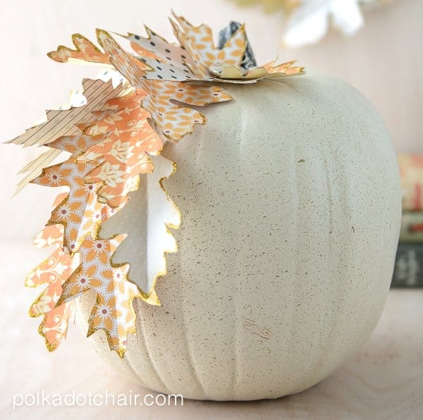 A white painted pumpkin with scrapbook paper leaves.