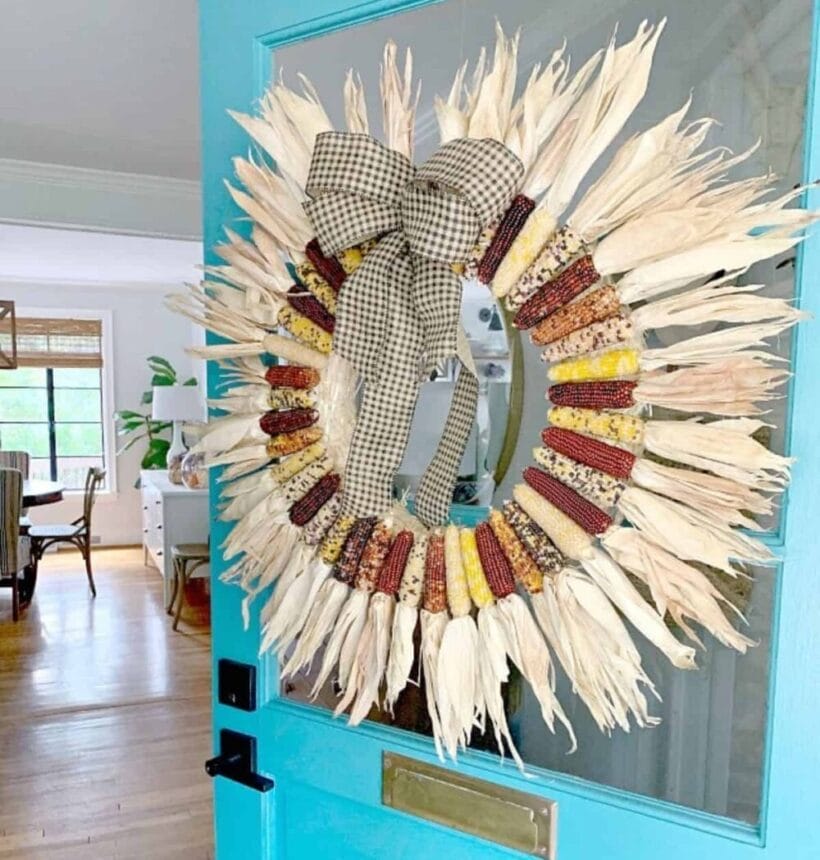 A wreath made of dried indian corn hung up on a bright ble door.
