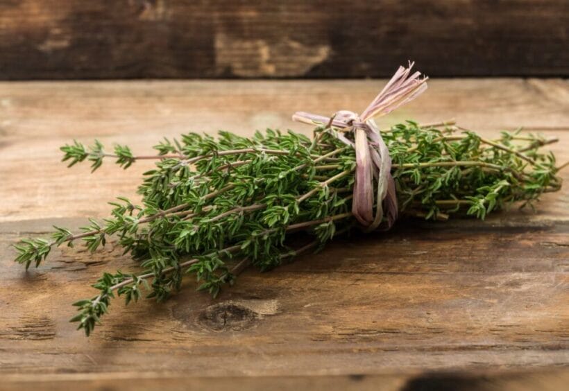 Sprigs of thyme wrapped in twine on a cutting board.