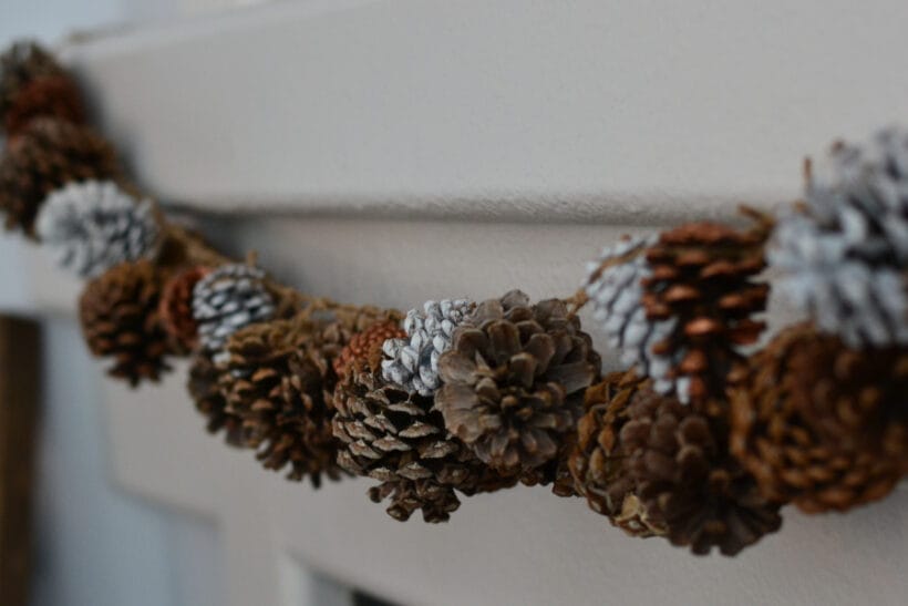A pinecone garland hung on a white painted mantle.