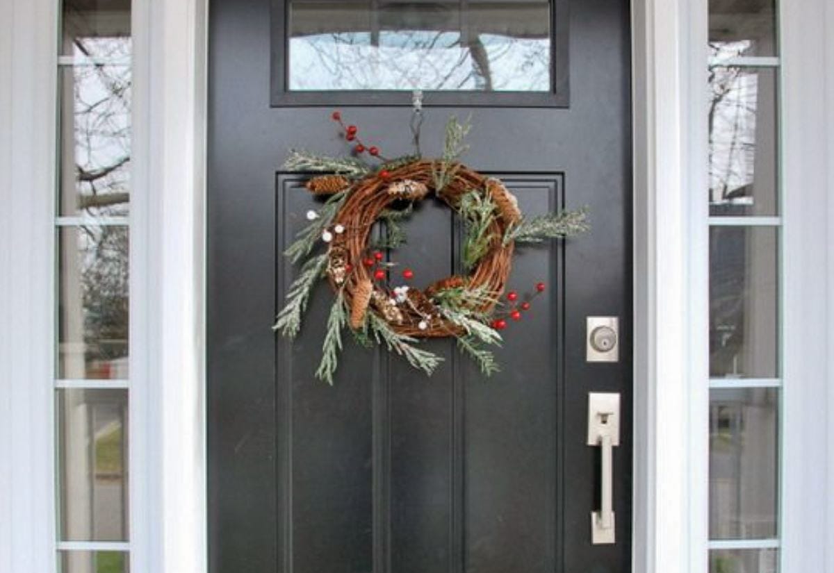Homemade grapevine Christmas wreath decorated with pine sprigs, pinecones, and red berries hanging on a dark front door.