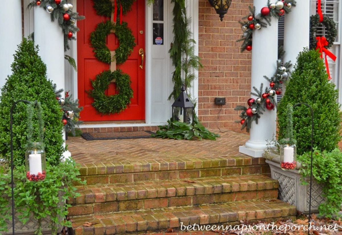 Outdoor Christmas entryway with garland, wreaths, and mason jar lanterns filled with cranberries and white candles lining brick steps.