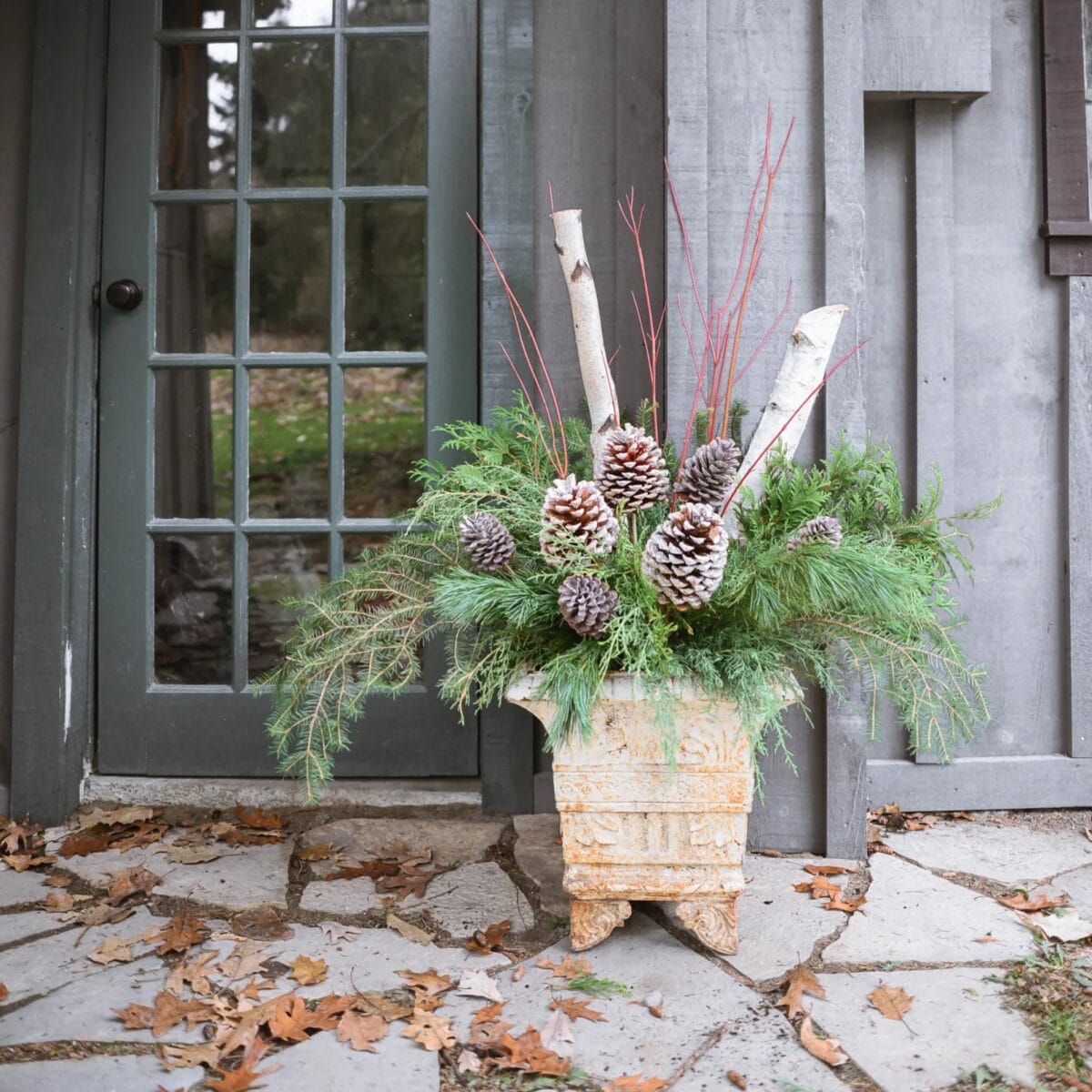A festive floral planter with evergreen boughs, birch limbs, and pinecones.