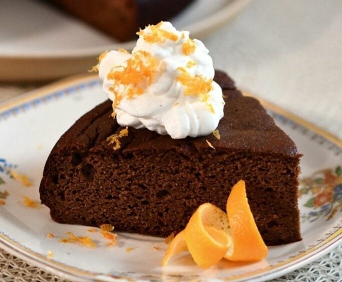 A slice of orange and chocolate almond cake with whipped cream and orange zest.