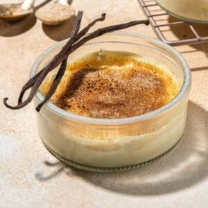 A glass ramekin of creme brulee with vanilla beans placed on top.