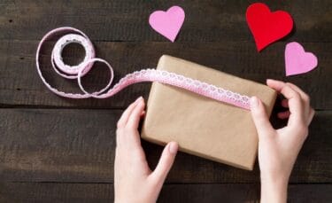 A woman wrapping a gift in brown paper and ribbon.