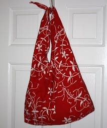 A red pillowcase shoulder bag with white floral pattern hung up on a door.