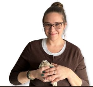 A headshot of Jessica Knowles holding a coturnix quail. Jessica is wearing a brown cardigan and has her hair up in a messy bun.