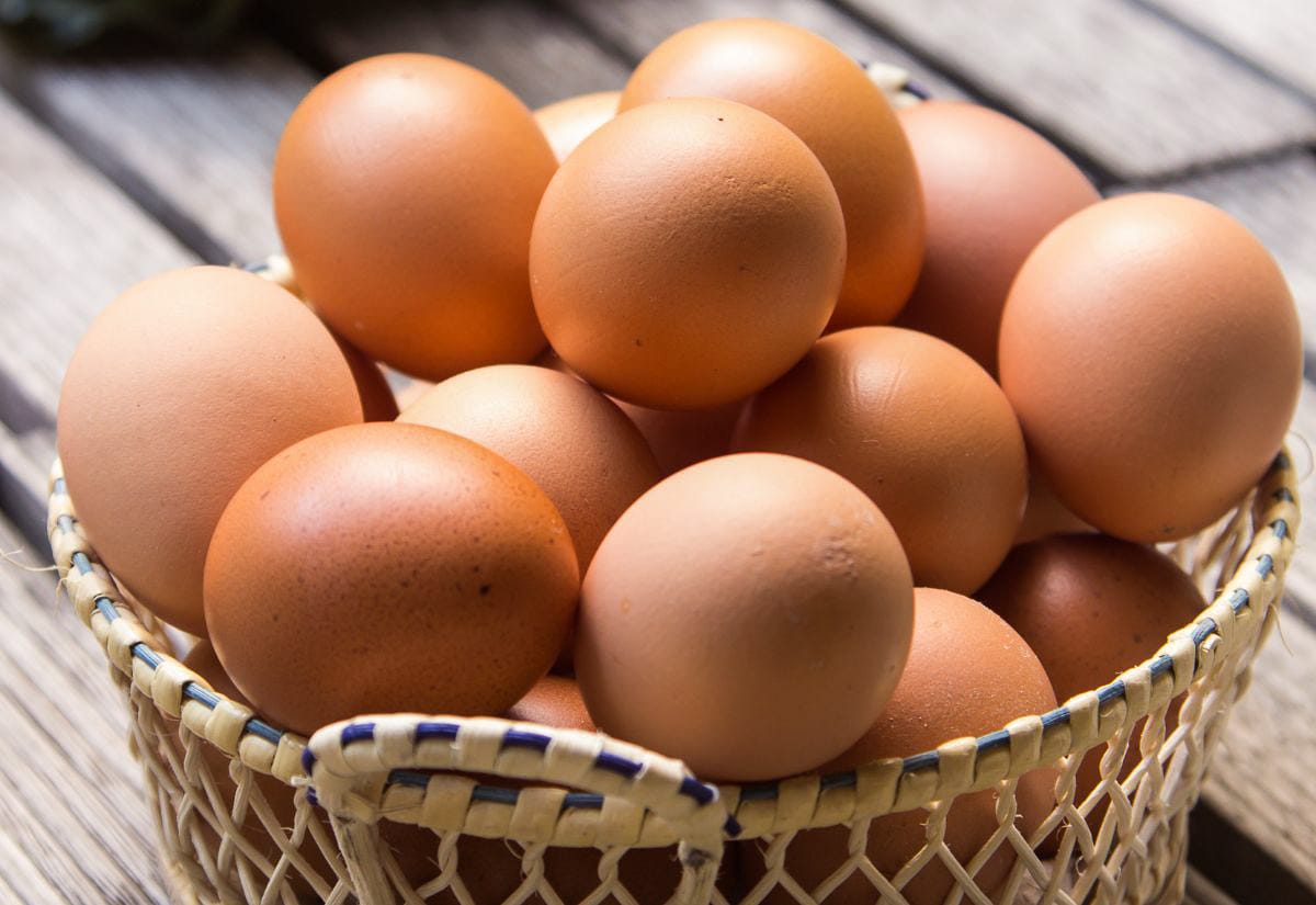 A woven basket filled with fresh brown eggs on a wooden surface.