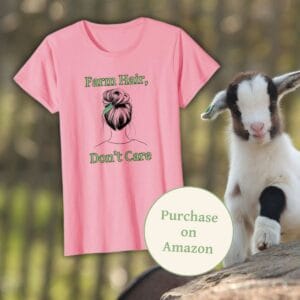 A pink Farm Hair, Don’t Care t-shirt displayed against a rustic farm setting, with a playful baby goat beside it. The shirt features a trendy messy bun with a feather accent and green lettering, perfect for farm-loving women. A "Purchase on Amazon" badge is included for easy shopping.