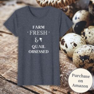 A heathered navy blue t-shirt with the phrase "Farm Fresh & Quail Obsessed" in white text, featuring a small quail silhouette. The shirt is displayed against a rustic wooden background with speckled quail eggs in a basket. A circular badge in the bottom right corner reads "Purchase on Amazon."