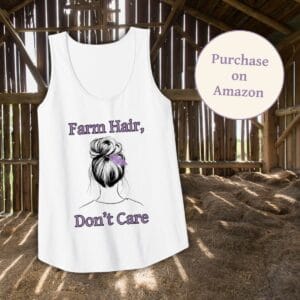 A white Farm Hair, Don’t Care tank top displayed in a rustic barn setting. The shirt features a stylish messy bun design with a feather accent, reflecting a relaxed farm lifestyle. A "Purchase on Amazon" badge is included, directing customers to the product listing.