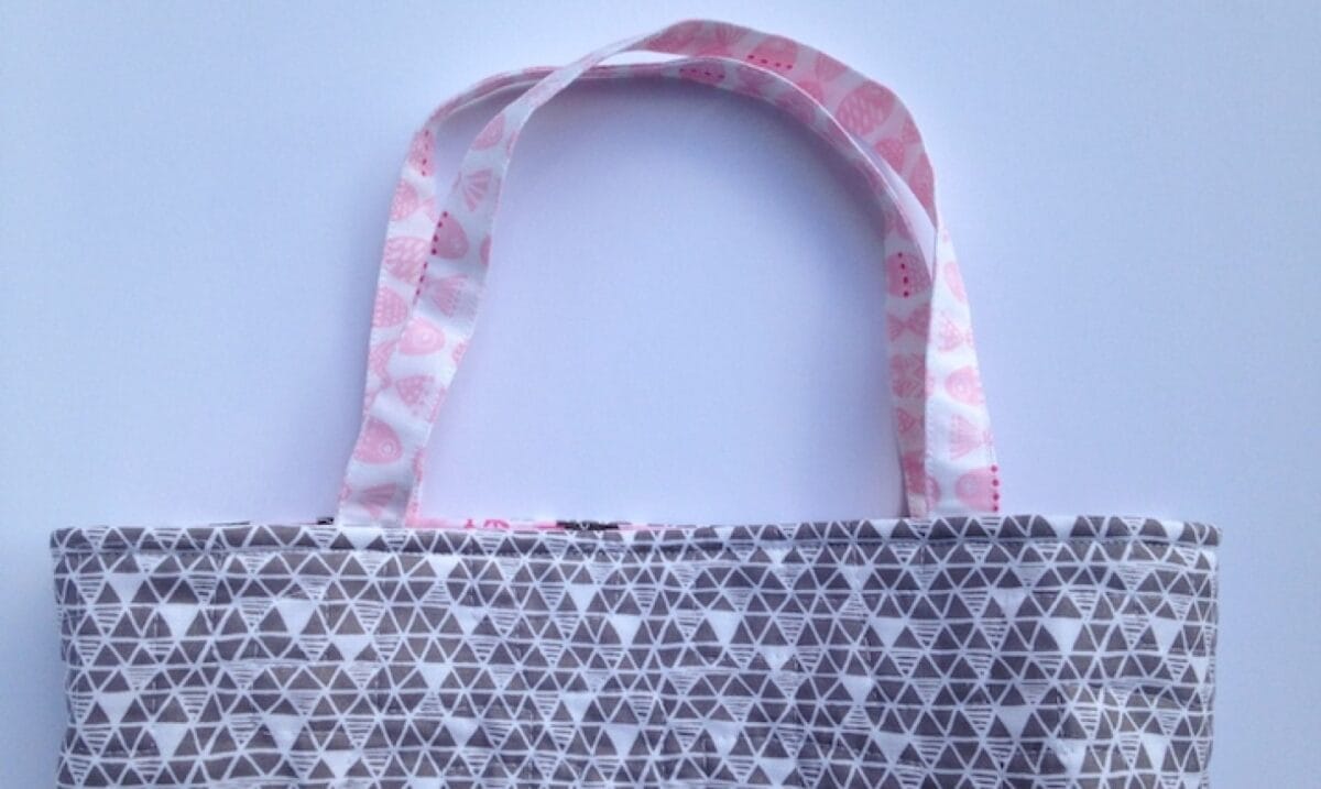A gray and white quilted tote bag with pink heart handles.