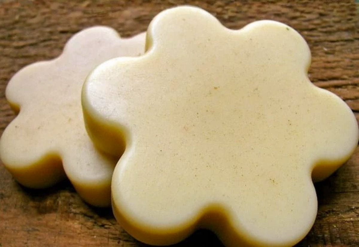 Two handmade beeswax lotion bars molded into simple flower shapes, resting on a rustic wooden surface.