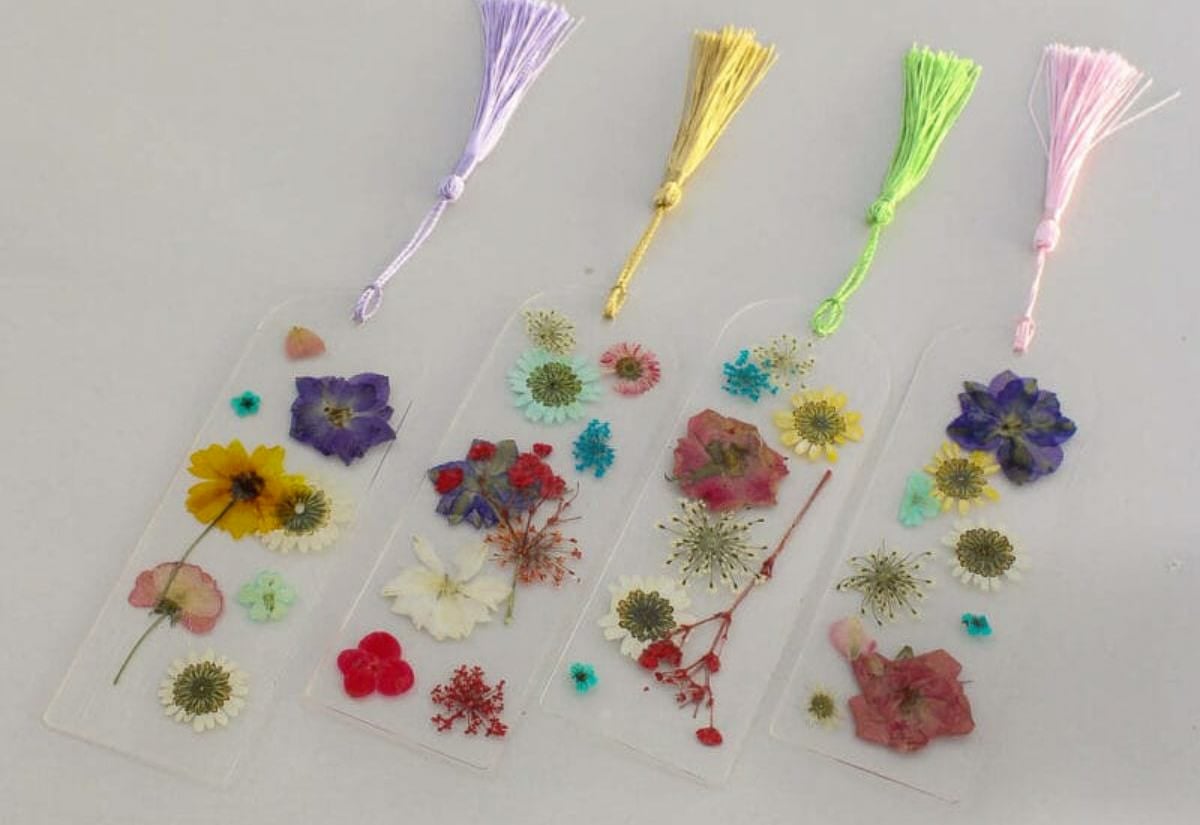 A row of clear resin bookmarks decorated with colorful pressed flowers and finished with pastel tassels.