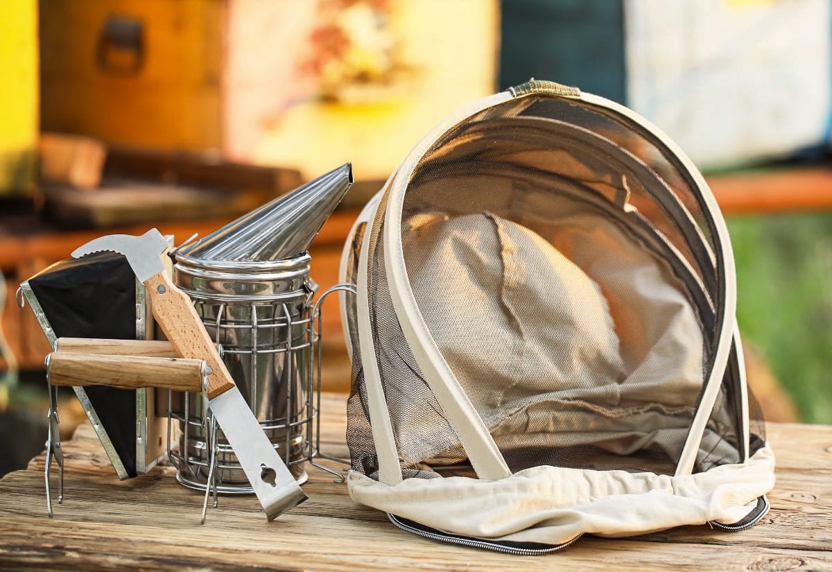 Basic beekeeping tools and protective veil resting on a wooden table near active beehives