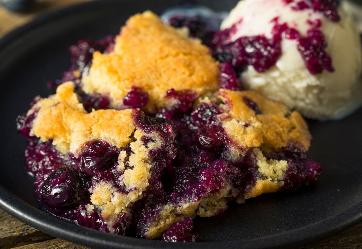 A closeup view of my homemade blueberry cobbler with a scoop of vanilla ice cream in the background.