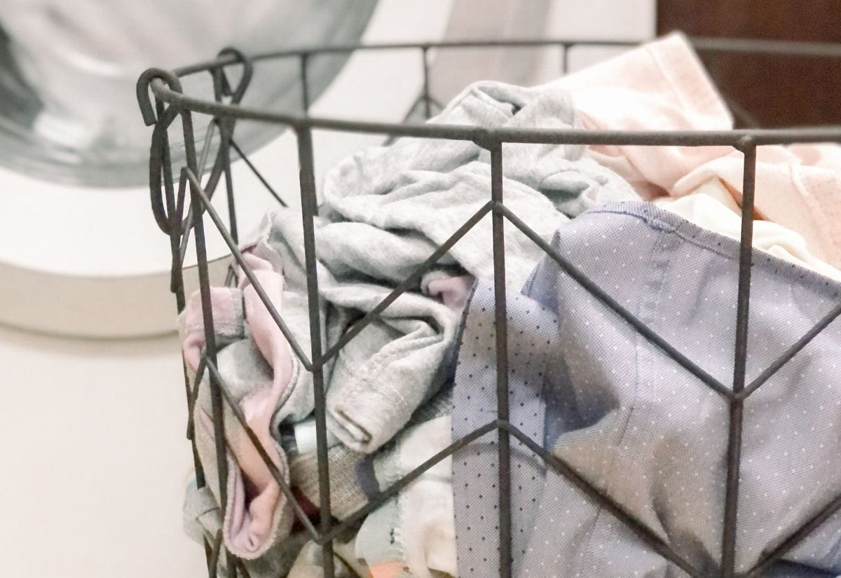 Dirty laundry in a wire basket sitting in front of a washing machine.