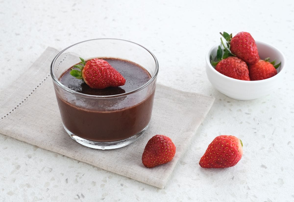 A glass of avocado chocolate pudding garnished with a fresh strawberry, with extra strawberries on the side.